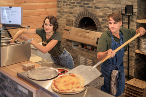 Dos personas preparan pizza en una cocina del parque vacacional Huttopia De Meinweg en Limburgo, Países Bajos, junto a un horno.