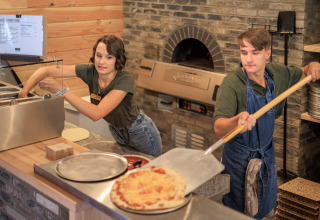 Twee mensen bereiden pizza in de keuken van Huttopia De Meinweg vakantiepark in Limburg, Nederland, dicht bij een oven.