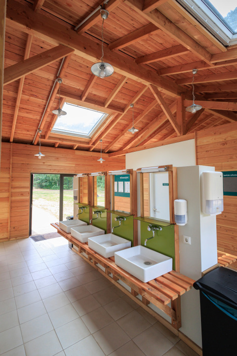 Modern gemeenschappelijk sanitair met houten plafond en wastafels bij Huttopia De Meinweg, Limburg.
