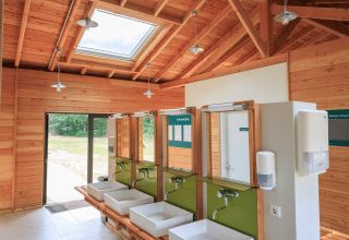 Modern gemeenschappelijk sanitair met houten plafond en wastafels bij Huttopia De Meinweg, Limburg.