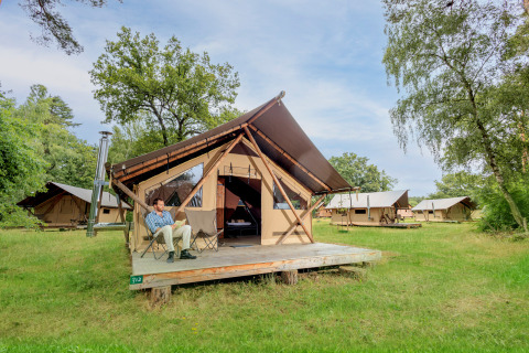 Hombre relajándose frente a una tienda glamping en Huttopia De Meinweg, Limburg, Países Bajos, rodeado de naturaleza.