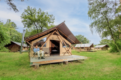 Homme assis devant une tente glamping au parc de vacances Huttopia De Meinweg, Limbourg, Pays-Bas, en pleine nature.