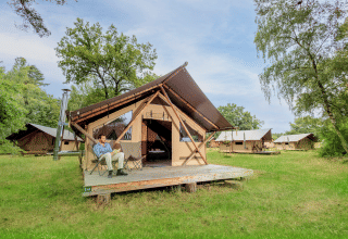 Uomo rilassato davanti a una tenda glamping a Huttopia De Meinweg, Limburg, Paesi Bassi, immerso nella natura.