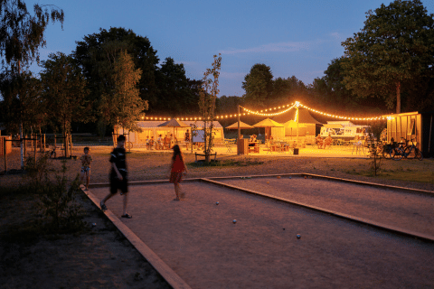 Atardecer en Huttopia De Meinweg en Limburg, Países Bajos, con luces decorativas y gente jugando petanca.