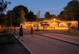 Abendstimmung bei Huttopia De Meinweg, Limburg mit Lichterketten und Menschen beim Petanque-Spielen.