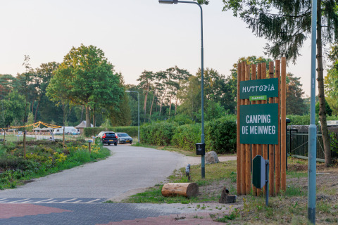 Entrada al parque vacacional Huttopia De Meinweg en Limburg, Países Bajos, con letrero y autos estacionados.