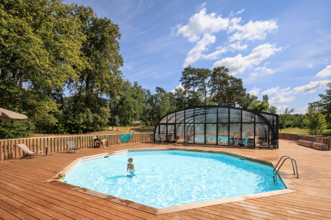 Piscina al aire libre con terraza de madera y zona cubierta en Huttopia De Meinweg, Limburg, Países Bajos.