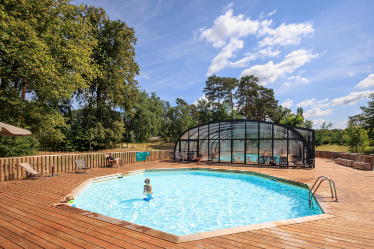 Outdoor swimming pool with wooden deck and covered pool area at Huttopia De Meinweg holiday park, Limburg, Netherlands.