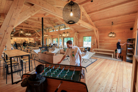 Holzinterieur im Gemeinschaftsraum des Ferienparks Huttopia De Meinweg, Menschen spielen Tischfußball.