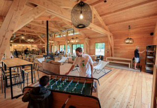 Holzinterieur im Gemeinschaftsraum des Ferienparks Huttopia De Meinweg, Menschen spielen Tischfußball.