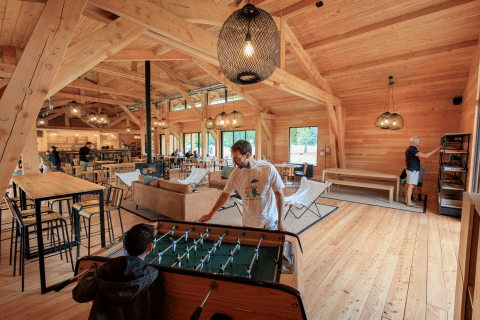 Houten gemeenschapsruimte in Huttopia De Meinweg, mensen ontspannen en spelen tafelvoetbal samen.