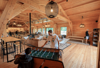 Houten gemeenschapsruimte in Huttopia De Meinweg, mensen ontspannen en spelen tafelvoetbal samen.