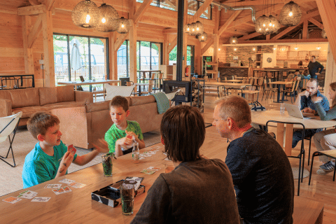 Families enjoying card games and relaxation in a cozy communal lounge at Huttopia De Meinweg holiday park.