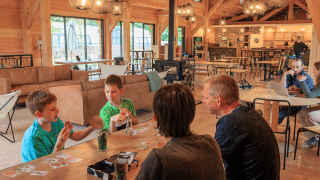 Familias jugando a las cartas y relajándose en una sala común acogedora en Huttopia De Meinweg, Limburg.