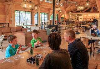 Familias jugando a las cartas y relajándose en una sala común acogedora en Huttopia De Meinweg, Limburg.