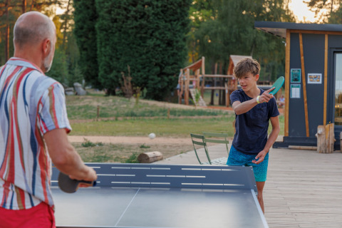 Un hombre y un niño juegan al tenis de mesa al aire libre en Huttopia De Meinweg en Limburg, Países Bajos.