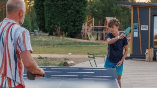 Un hombre y un niño juegan al tenis de mesa al aire libre en Huttopia De Meinweg en Limburg, Países Bajos.