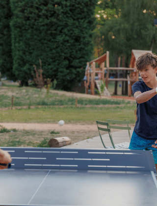 Un hombre y un niño juegan al tenis de mesa al aire libre en Huttopia De Meinweg en Limburg, Países Bajos.