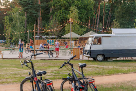 Escena al aire libre en Huttopia De Meinweg, Limburg, Países Bajos con personas, bicicletas y luces decorativas.