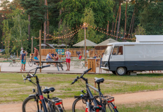 Buitenscène aan Huttopia De Meinweg, Limburg, Nederland met mensen, fietsen en lichtslingers.