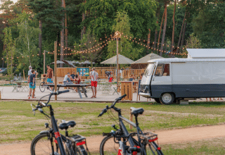 Outdoor scene at Huttopia De Meinweg holiday park in Limburg, Netherlands with people, bikes and string lights.