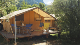 Bungalow tent Classic safari tent with wooden deck, camping chairs and table in scenic outdoors.