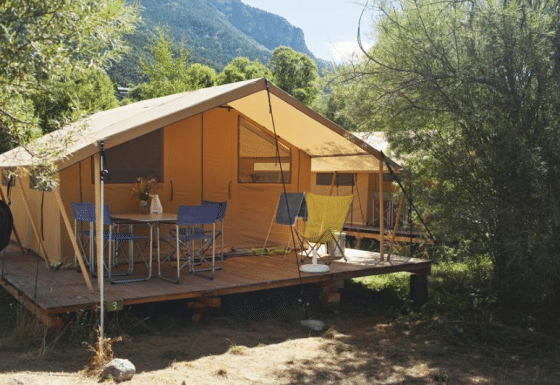 Bungalow tent Classic safaritent met houten terras, campingstoelen en tafel in groene omgeving.