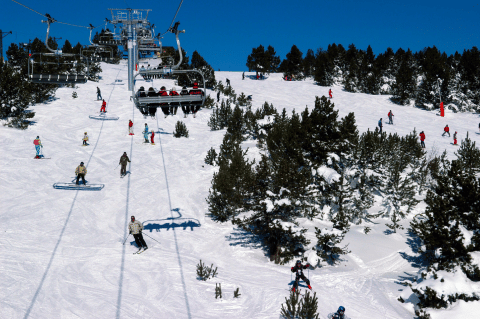 Skiers and chairlift on a snowy slope surrounded by pine trees at Les Chalets Huttopia de Vallouise, France.