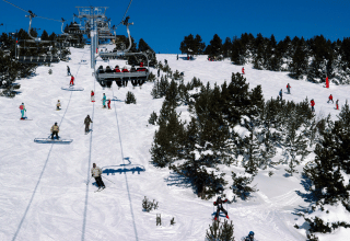 Skiers and chairlift on a snowy slope surrounded by pine trees at Les Chalets Huttopia de Vallouise, France.