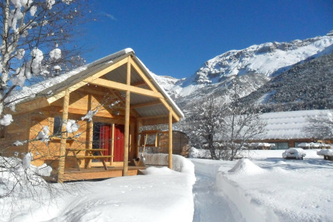 Houten chalet in de sneeuw bij Les Chalets Huttopia de Vallouise met bergen op de achtergrond, Zuid-Frankrijk.