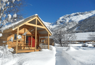 Chalet en bois sous la neige à Les Chalets Huttopia de Vallouise avec vue sur les montagnes dans les Alpes françaises.