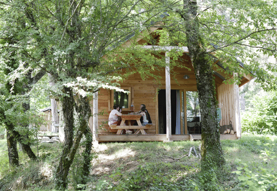 Dos personas sentadas en una mesa fuera del Chalet Montana en Huttopia Vallouise, Francia, rodeadas de árboles.