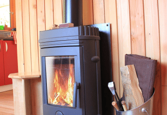 Estufa de leña encendida junto a cubo con leña y pared de madera en Chalet Montana, Huttopia Vallouise.