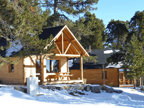 Wooden cabins in snowy forest setting at Les Chalets Huttopia de Font-Romeu holiday park in Occitanie, France.