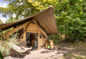 Das Safari-Zelt Canadienne mit Holzterrasse und Campingstühlen, umgeben von grünen Wald und Natur.