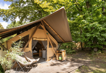 Tente safari Canadienne avec terrasse en bois et fauteuils, entourée d’arbres verts dans la forêt.