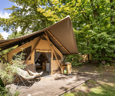 Das Safari-Zelt Canadienne mit Holzterrasse und Campingstühlen, umgeben von grünen Wald und Natur.