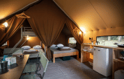 Interieur van een gezellige safaritent genaamd Canadienne bij Huttopia Versailles in Frankrijk, met bedden en keuken.