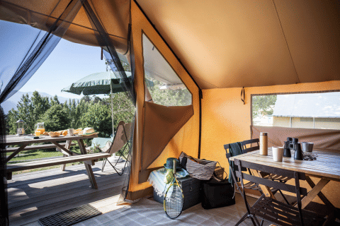 Blick aus einem Safari-Zelt bei Huttopia Versailles, mit Gartenmöbeln und Picknicktisch draußen.