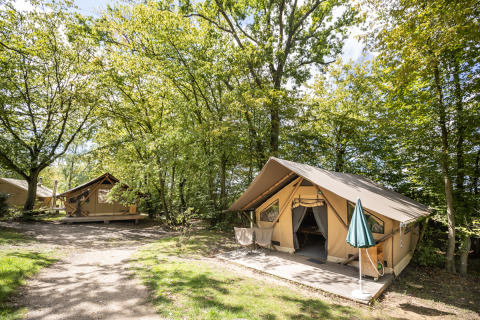 Tienda safari Trappeur sobre una plataforma de madera en un camping rodeado de árboles y naturaleza.