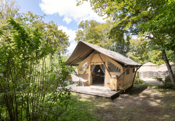 The Trappeur safari tent at Huttopia Versailles in France, nestled in green forest with sun and nature around.