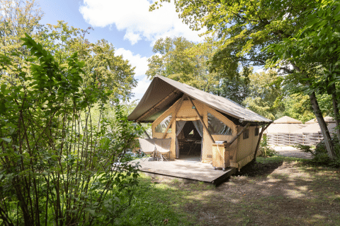 Das Safari-Zelt Trappeur bei Huttopia Versailles in Frankreich, umgeben von grüner Natur und Bäumen.