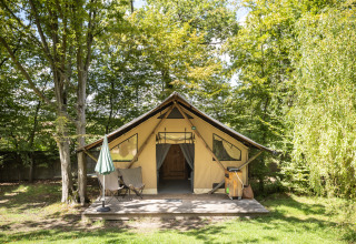 De Trappeur safaritent bij Huttopia Versailles in Frankrijk, tussen het groen met terras en stoelen.