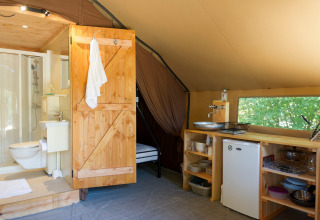 Vista interna di una tenda safari con piccola cucina, frigorifero e bagno privato con doccia.