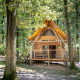 Die Waldhütte Cahutte besteht aus Holz und hat ein gelbes Dach. Sie liegt umgeben von hohen Bäumen.