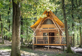 Die Waldhütte Cahutte besteht aus Holz und hat ein gelbes Dach. Sie liegt umgeben von hohen Bäumen.