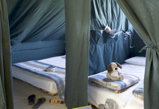 Inside a Cahutte at Huttopia Versailles, France, featuring two beds with blankets, toys, and a cozy camping setup.