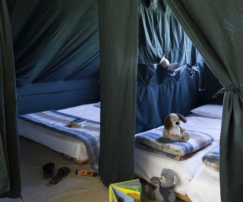 Interior de una Cahutte en Huttopia Versailles, Francia, con dos camas, mantas, juguetes y ambiente acogedor.