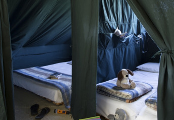 Innenansicht einer Cahutte im Huttopia Versailles, Frankreich, mit zwei Betten, Decken und Kuscheltieren.