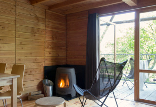 Cozy wooden cabin interior at Cahutte, Huttopia Versailles, France, featuring a fireplace and balcony.